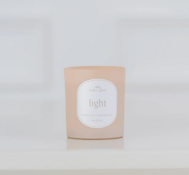 A frosted, light pinkish-beige candle in a glass jar sits on a white surface. The label reads